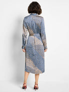 Midi-length shirt dress, long sleeves. Blue, beige, and white geometric print on dark background.  Back view.