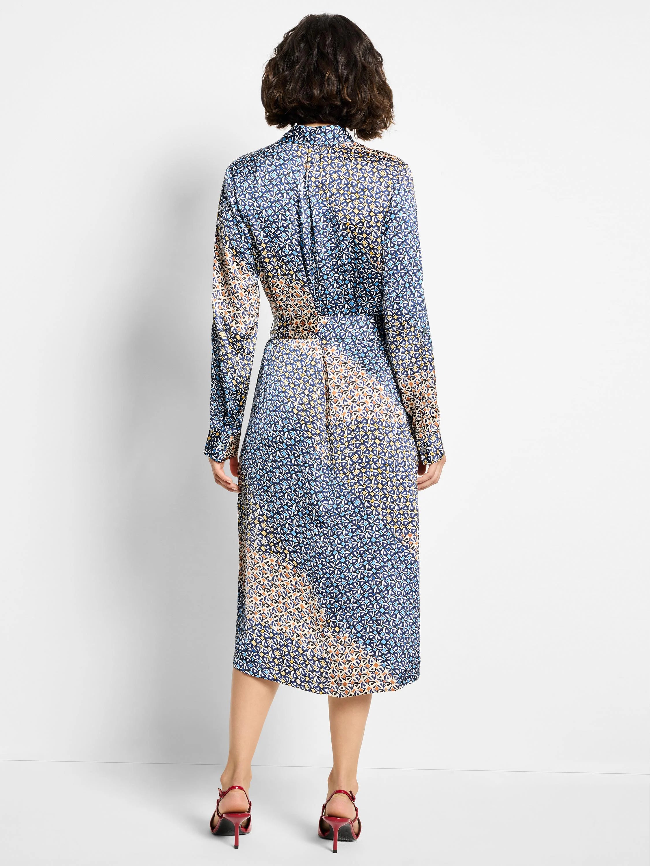Midi-length shirt dress, long sleeves. Blue, beige, and white geometric print on dark background.  Back view.