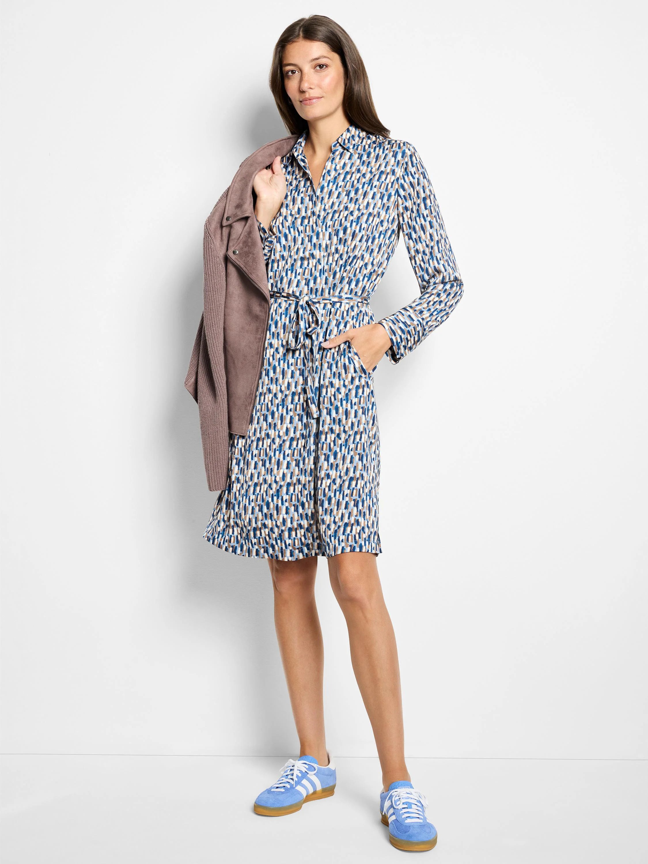 Long-sleeved knee-length dress, belted, in blue, beige, and white abstract print.  Model wears light blue sneakers.