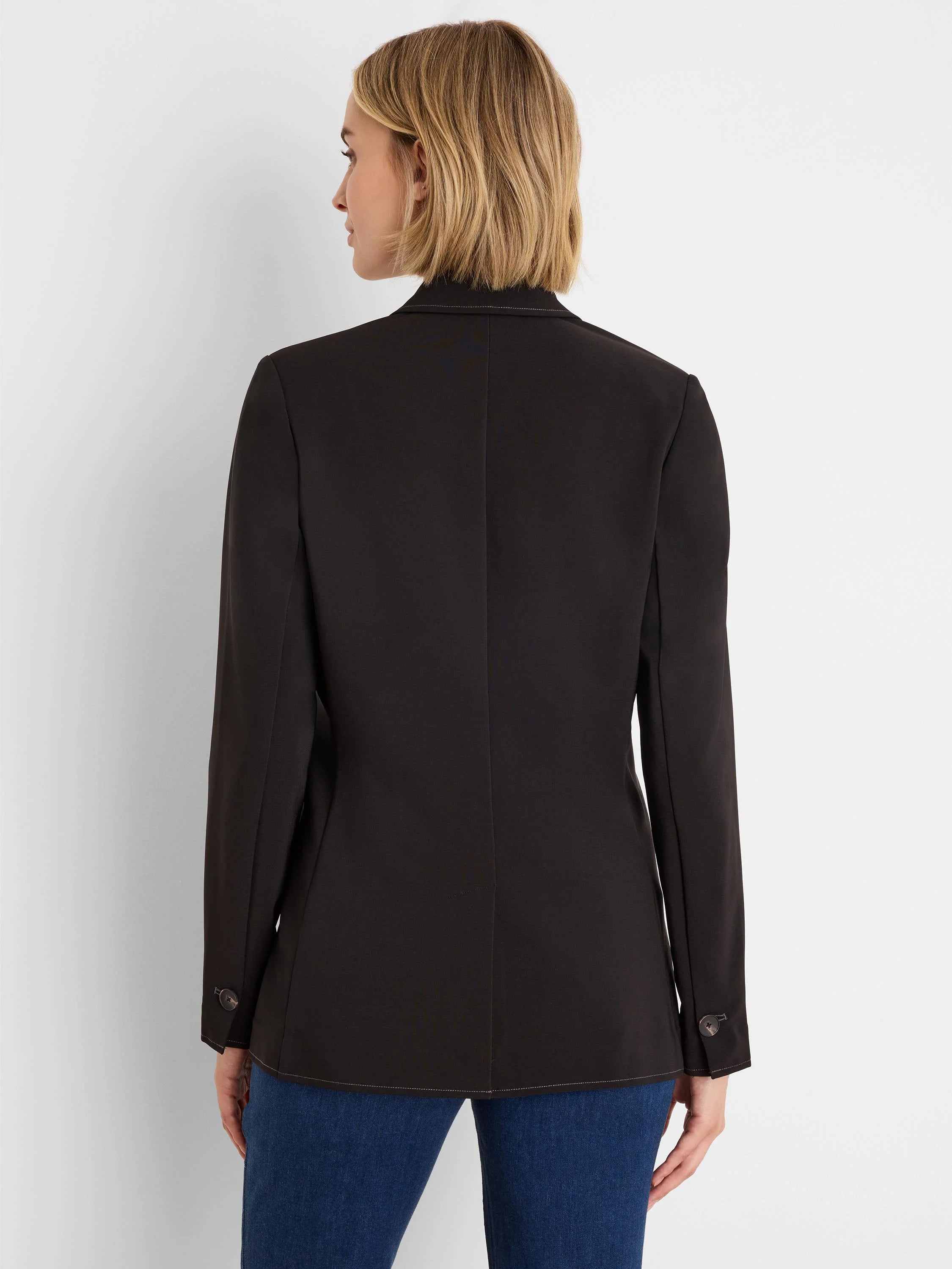 Black blazer, back view. Features light accent stitching along seams and hem, with two dark buttons on each cuff.