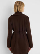 Dark brown wrap jacket, back view. Long sleeves; thin black belt cinches the waist, creating subtle folds.