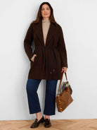 Dark brown knit twill wrap jacket with wide lapels, cinched with a thin dark belt, and reaching mid-thigh.