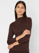 Model wears a dark brown, shimmering mock-neck long-sleeve top.