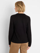 Black waffle-knit long-sleeve crew neck top on a model, seen from behind, wearing tan pants.