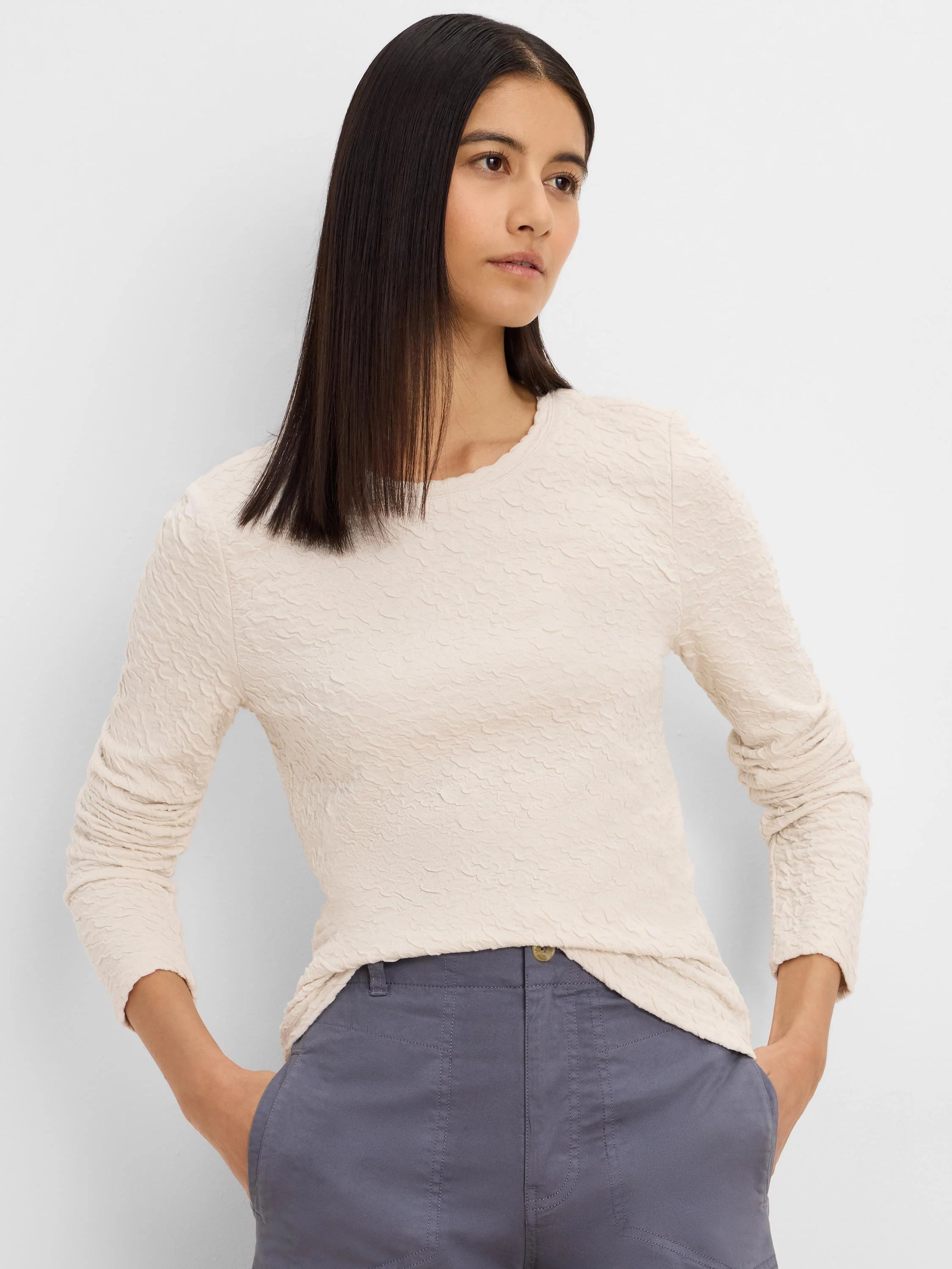 Pale beige, long-sleeved top with a round neck and distinct crinkle knit texture.