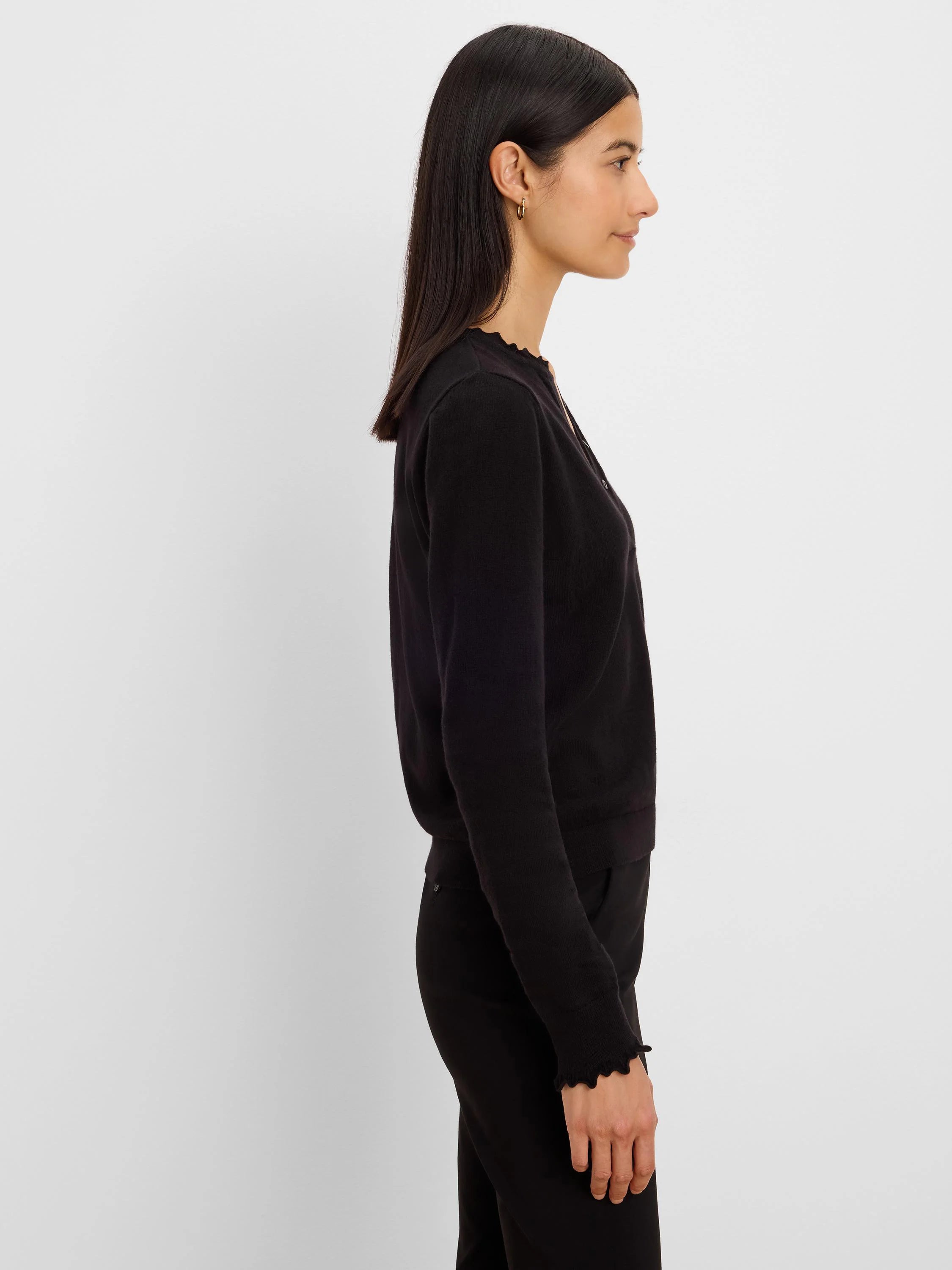 Black Henley sweater on model. Features ruffle trim on neckline and cuffs, and front buttons.