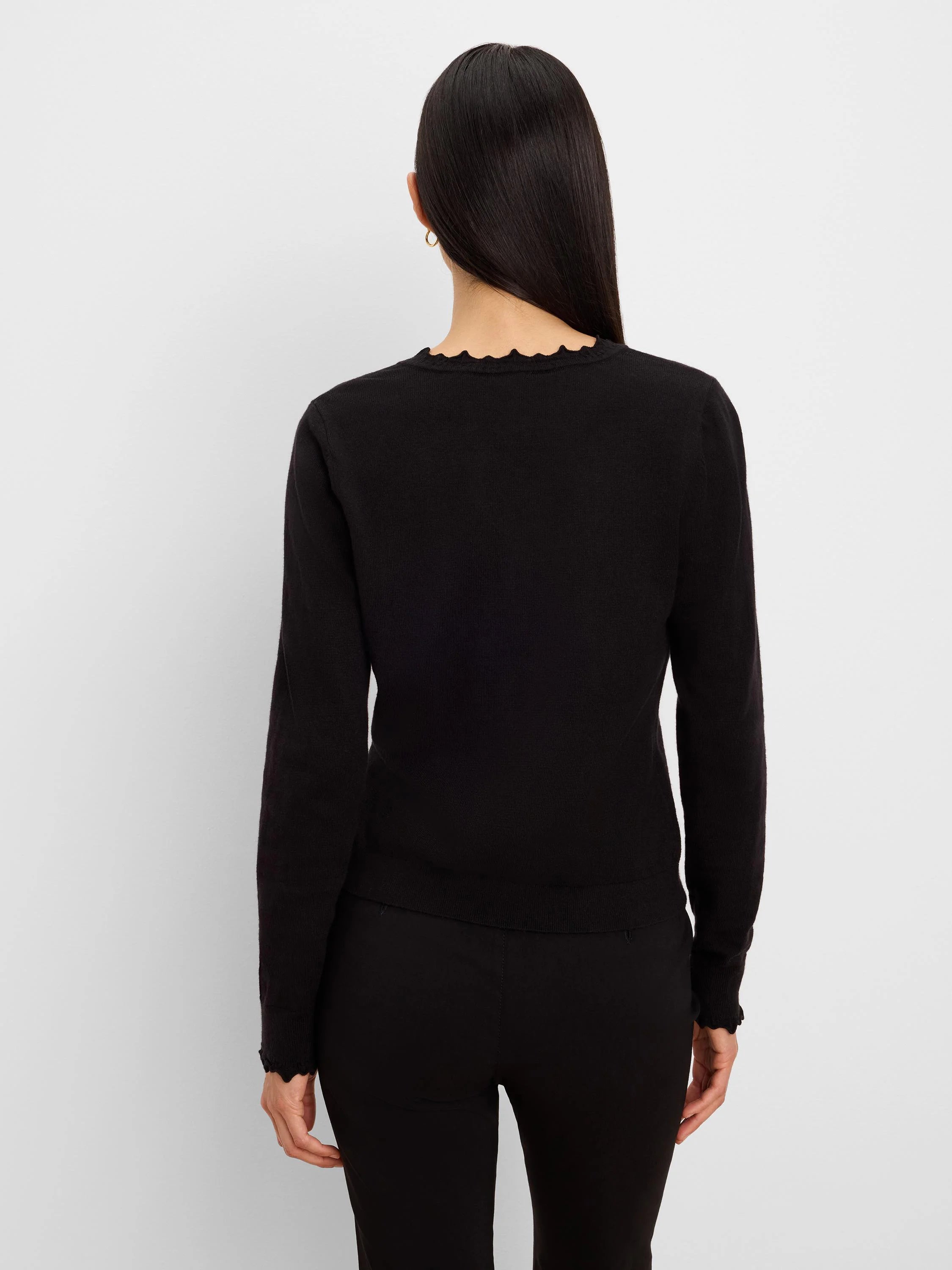 Black long-sleeved sweater, back view. Features a ruffled neckline and ruffled cuffs.