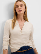 Cream Henley sweater with V-neck button placket, ruffled collar, and ruffled cuffs.