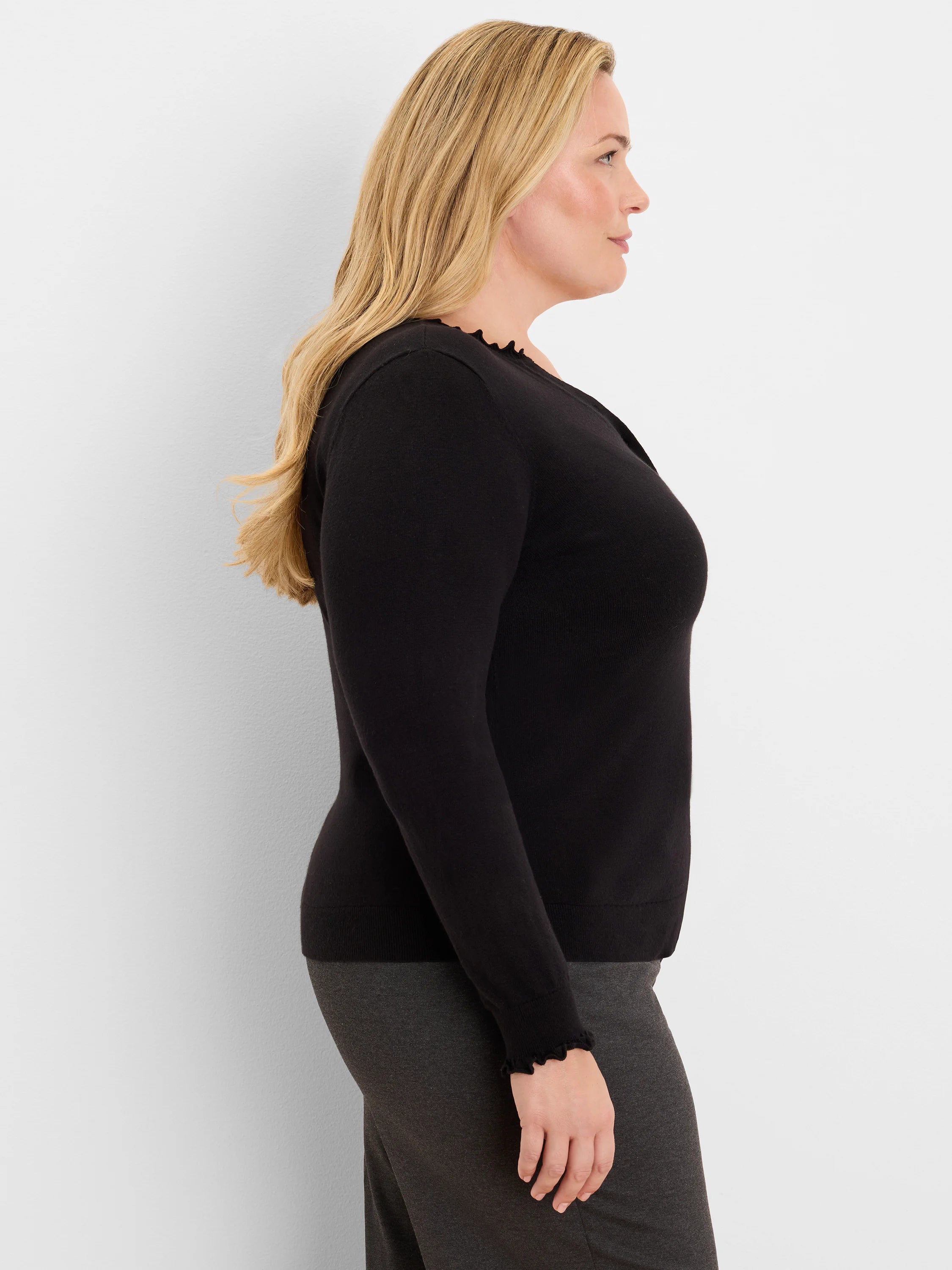 Black Henley sweater with long sleeves. Ruffle trim on the V-neckline and cuffs.
