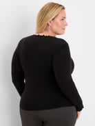 Black long-sleeve sweater with a ruffled crew neck and ruffled cuffs, worn by a model from the back-right.