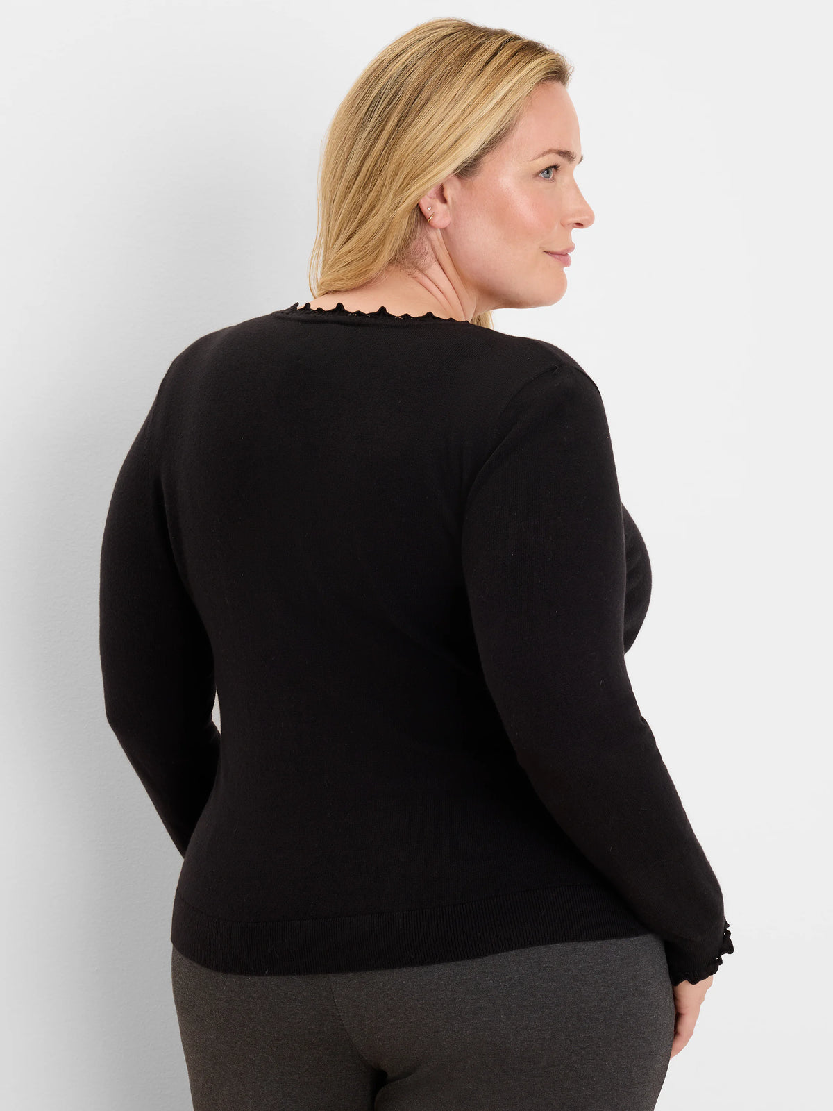 Black long-sleeve sweater with a ruffled crew neck and ruffled cuffs, worn by a model from the back-right.
