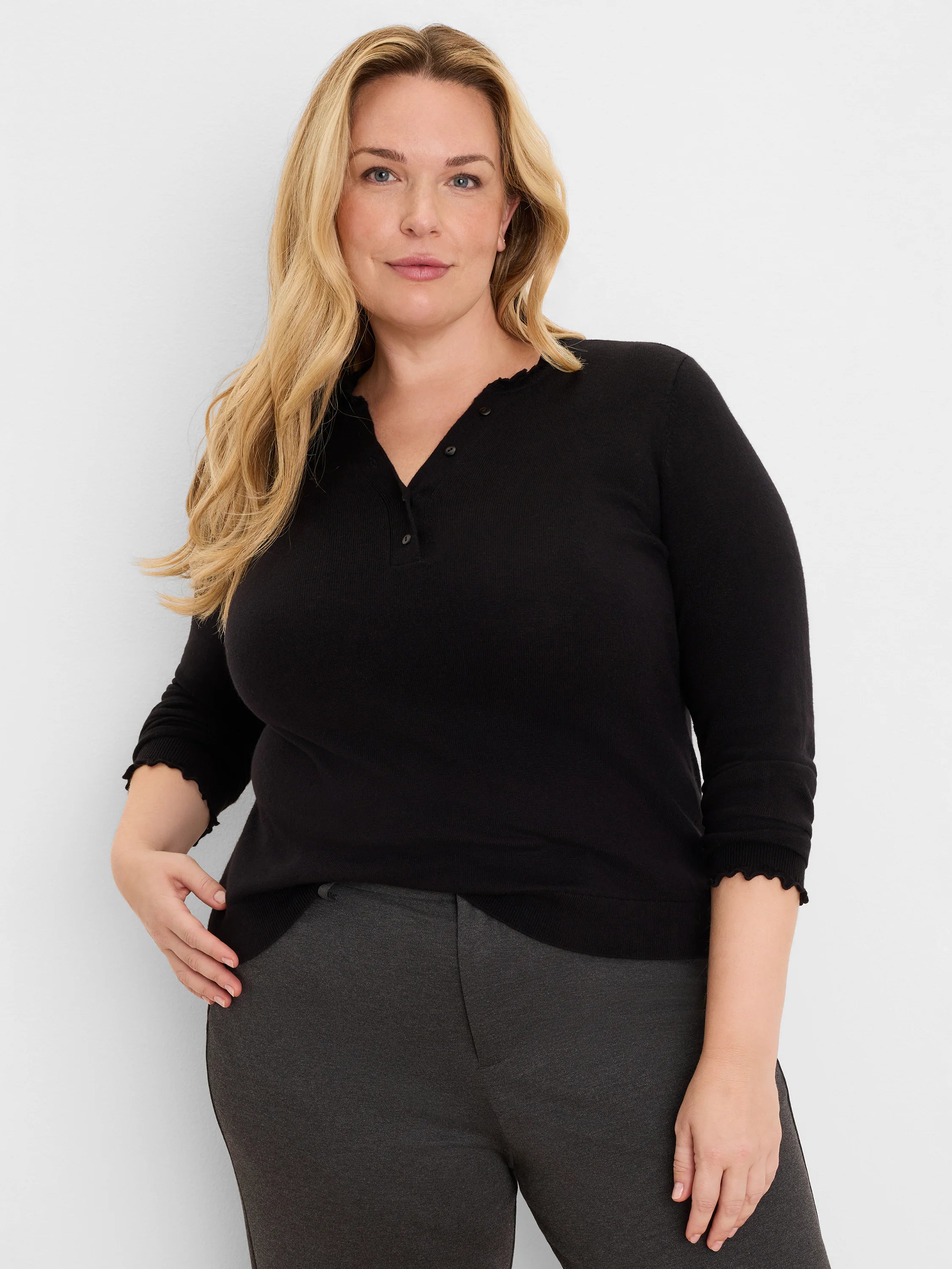 Black Henley sweater with ruffled v-neckline and 3/4 sleeves with ruffled cuffs.