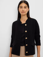 Black knit jacket with textured weave, gold buttons, collarless dark trim on the neckline and flap pockets.