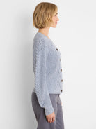 Light blue flecked shaker cardigan with cable knit sleeves and dark brown buttons, modeled from the side.