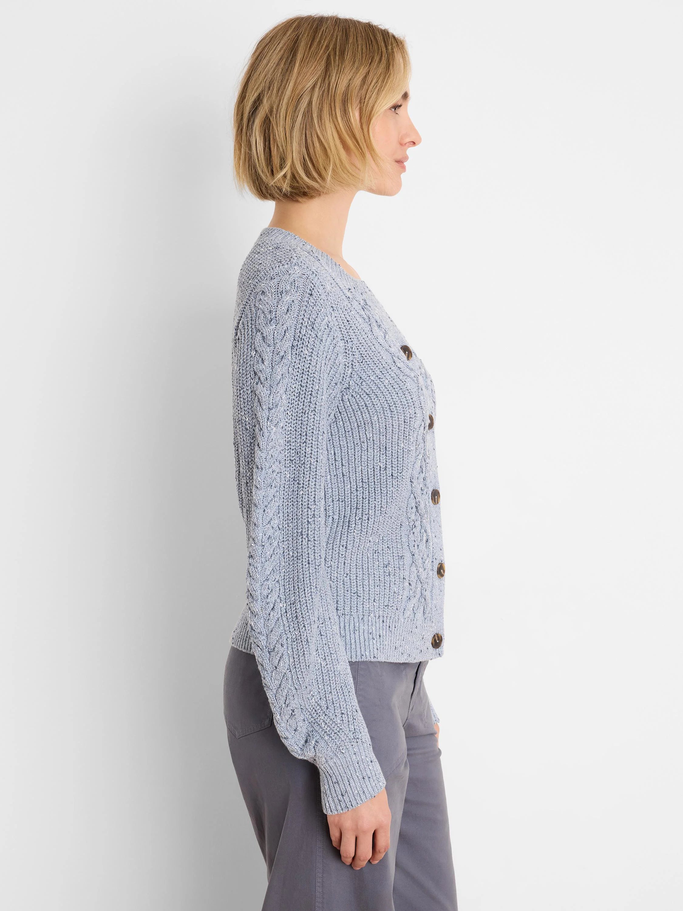 Light blue flecked shaker cardigan with cable knit sleeves and dark brown buttons, modeled from the side.