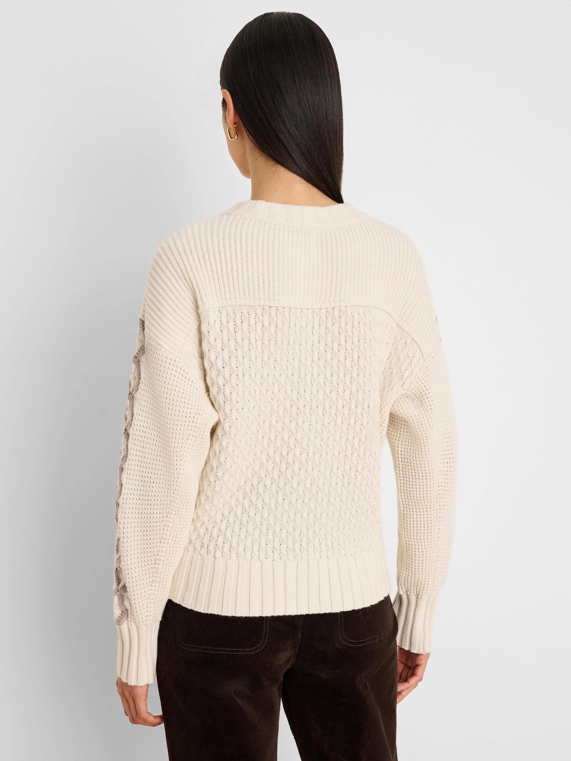 Cream cable knit sweater, back view. Tan criss-cross pattern on outer sleeves. Ribbed neck, cuffs, and hem.
