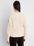 Cream cable knit sweater, back view. Tan criss-cross pattern on outer sleeves. Ribbed neck, cuffs, and hem.