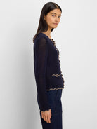 Navy open-knit cardigan with beige wavy trim on front, hem, cuffs, and faux pockets, plus small gold buttons.