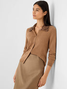 Camel knit button-front cardigan with a dark brown sequin collar. Model wears it with a tan skirt.