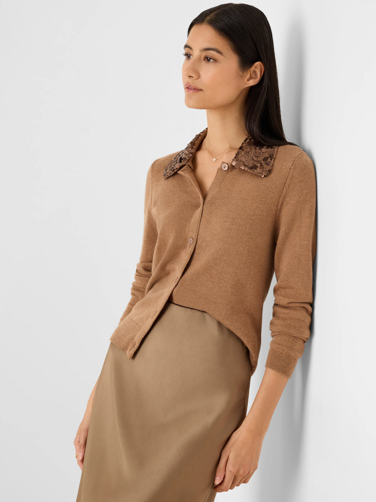 Camel knit button-front cardigan with a dark brown sequin collar. Model wears it with a tan skirt.