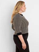 A woman wears a black and cream geometric knit sweater with lace trim at the neckline and 3/4 sleeves.