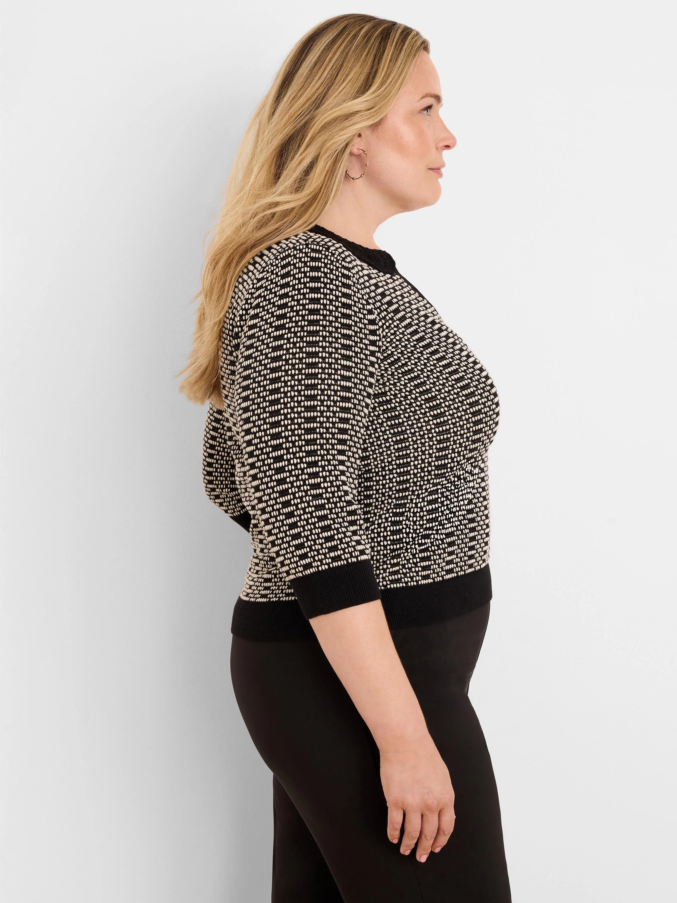 A woman wears a black and cream geometric knit sweater with lace trim at the neckline and 3/4 sleeves.
