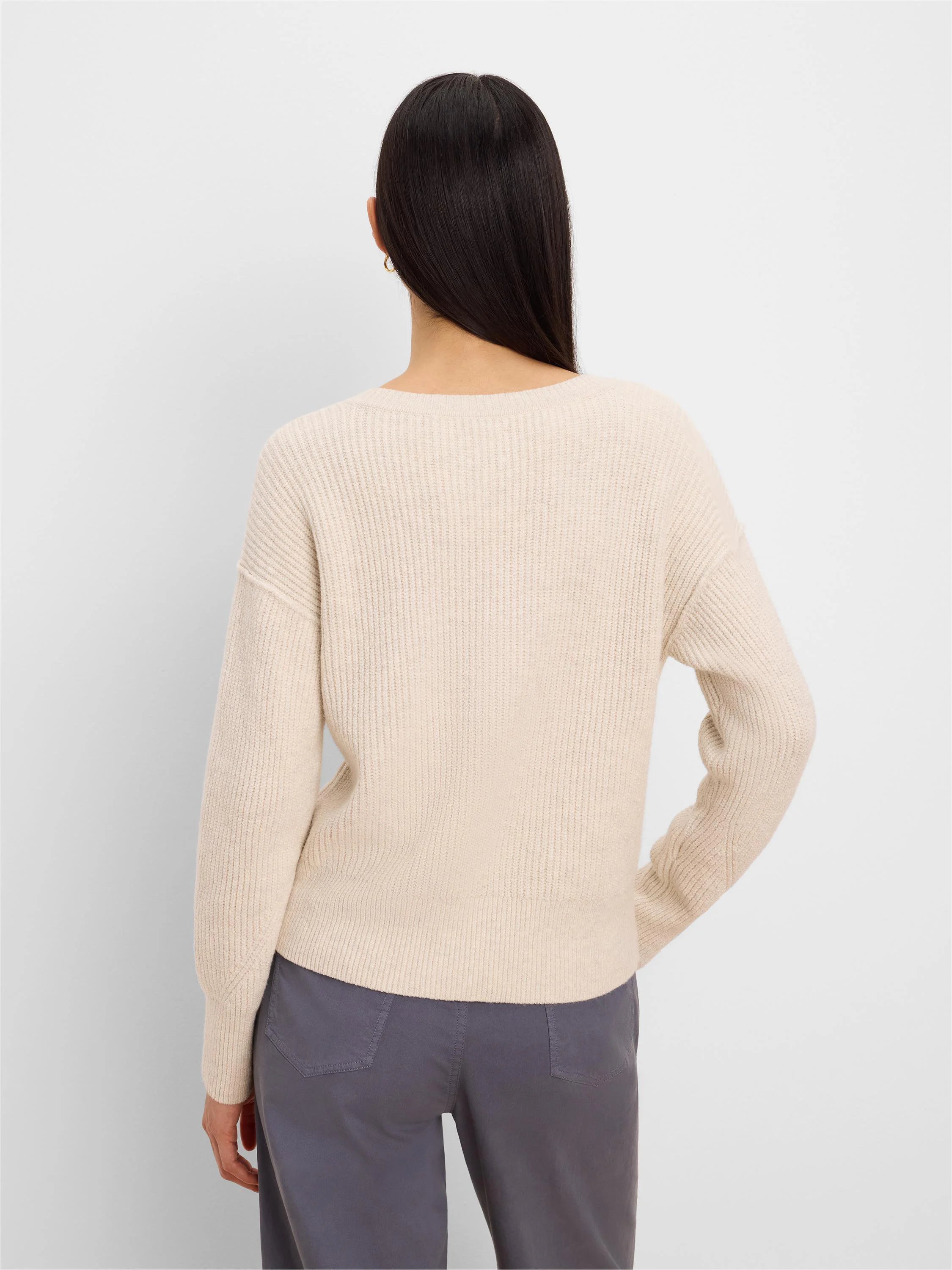 Light beige ribbed knit pullover sweater, shown from the back on a model. Features long sleeves and a relaxed fit.