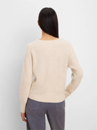Light beige ribbed knit pullover sweater, shown from the back on a model. Features long sleeves and a relaxed fit.