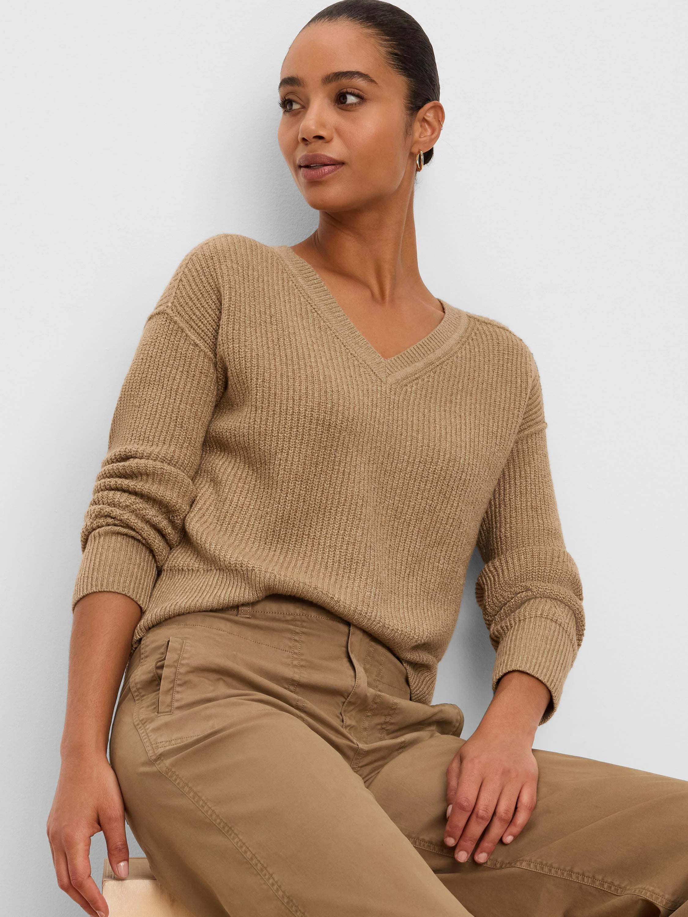 Model wearing a camel V-neck sweater with a distinct vertical ribbed knit pattern and ribbed cuffs.