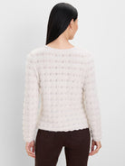 Ecru fuzzy knit sweater with openwork rows of small leaf-like patterns. Model from behind.