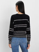 Black sweater with horizontal rows of white textured dots. White stripes on ribbed cuffs and hem.