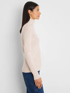 Light beige, form-fitting knit ribbed turtleneck with a folded neck and long sleeves.