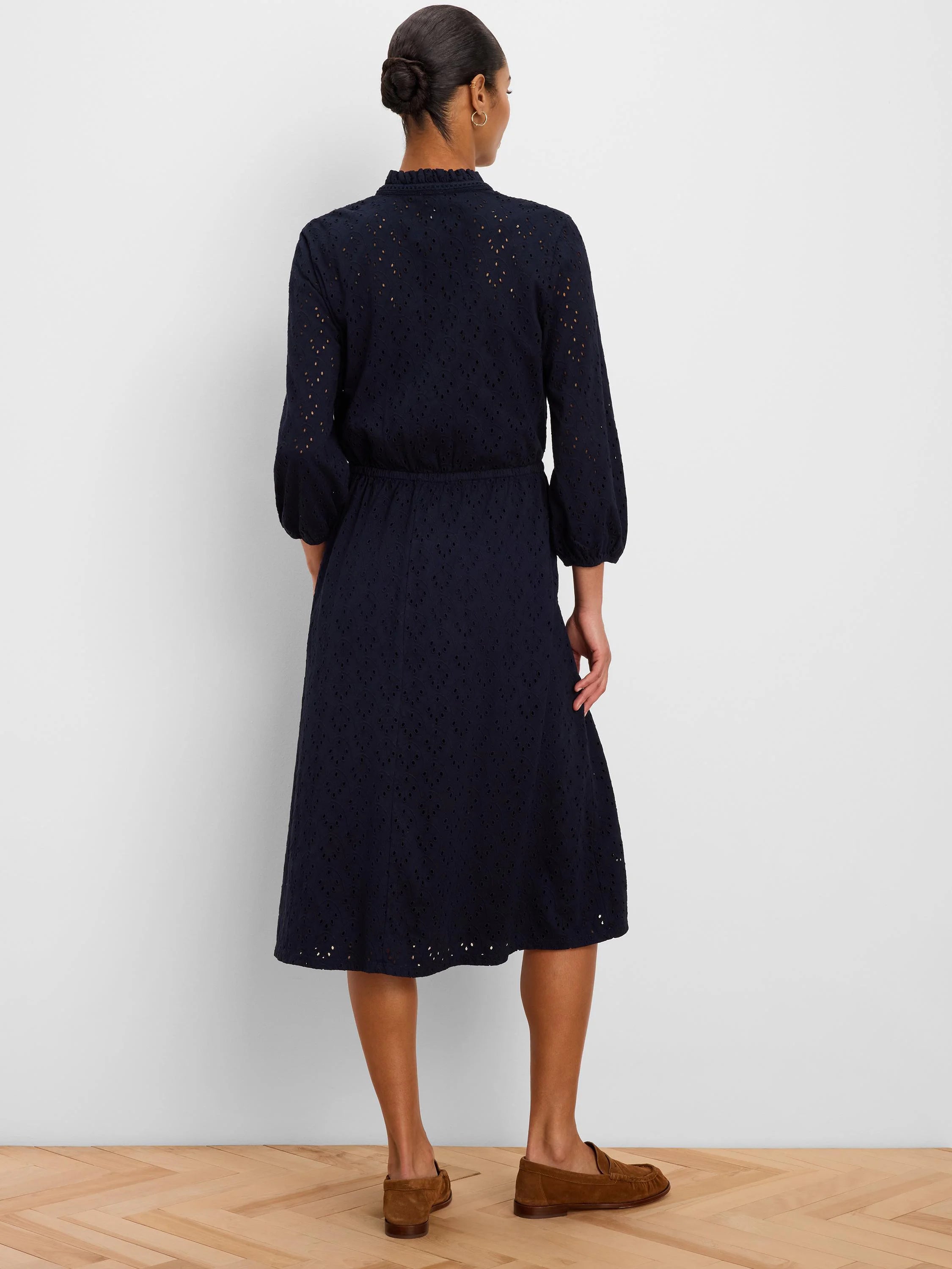 Navy eyelet midi dress with a ruffled mock neck, 3/4 sleeves, and smocked waist, shown from behind.