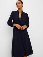 Dark blue midi dress with eyelet cut-out patterns, ruffled stand collar, V-neck, and long sleeves, worn by a model.