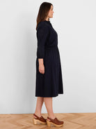 Navy eyelet midi dress with 3/4 sleeves, elastic waist, and ruffled collar, worn by a model.