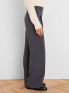 Dark grey wide-leg trousers, side view on a model. Smooth fabric, with a crisp front leg crease.