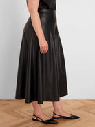 Black vegan leather midi A-line skirt with visible seams and a subtle sheen.