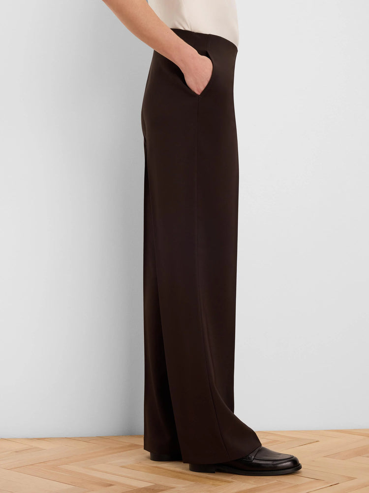 Dark brown wide-leg pants with a sleek finish, featuring a side slash pocket with a hand in it. Paired with a cream top.