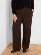 Dark brown wide-leg pants. Smooth fabric, full length, with a hand in one pocket.