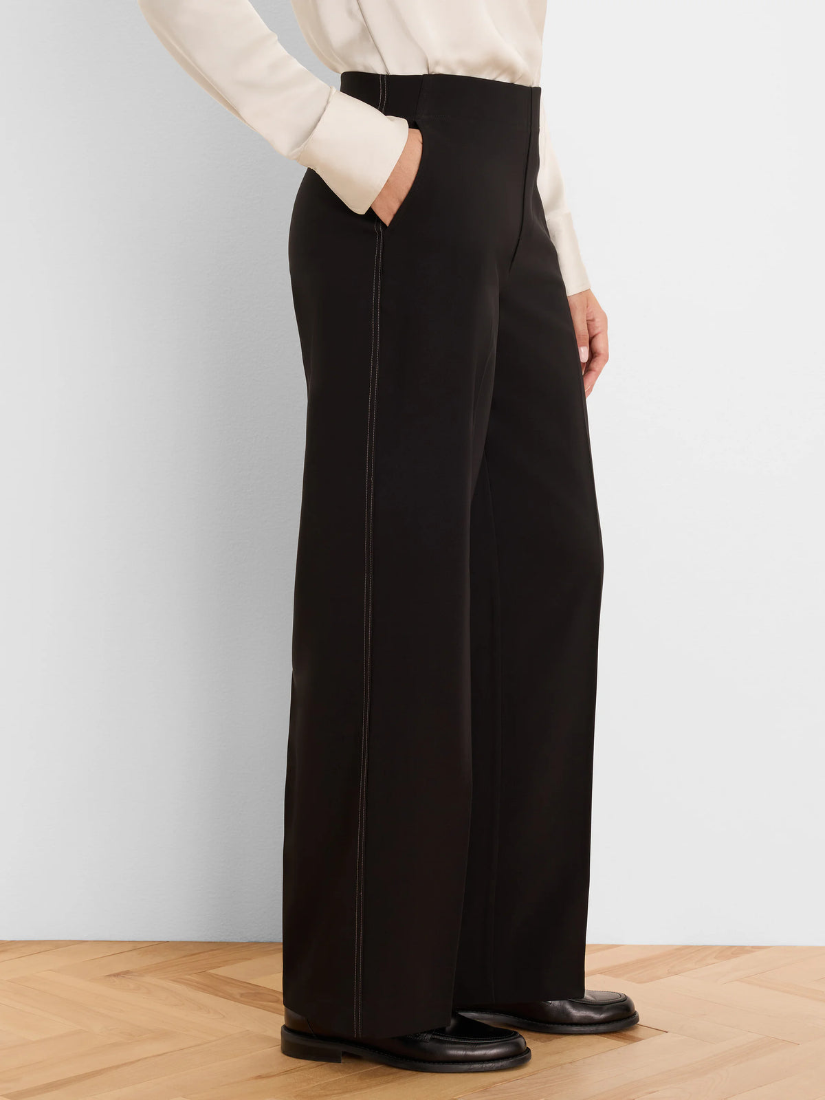 Black wide leg pants with light accent stitching on side seams and pockets. A hand is in one pocket.
