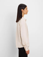 Light beige glossy shirt with a collar, long sleeves, and wide cuffs, worn by a model in profile.