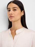 Light beige shirt with a stand collar and V-neck. Smooth fabric shows subtle sheen and visible collar stitching.