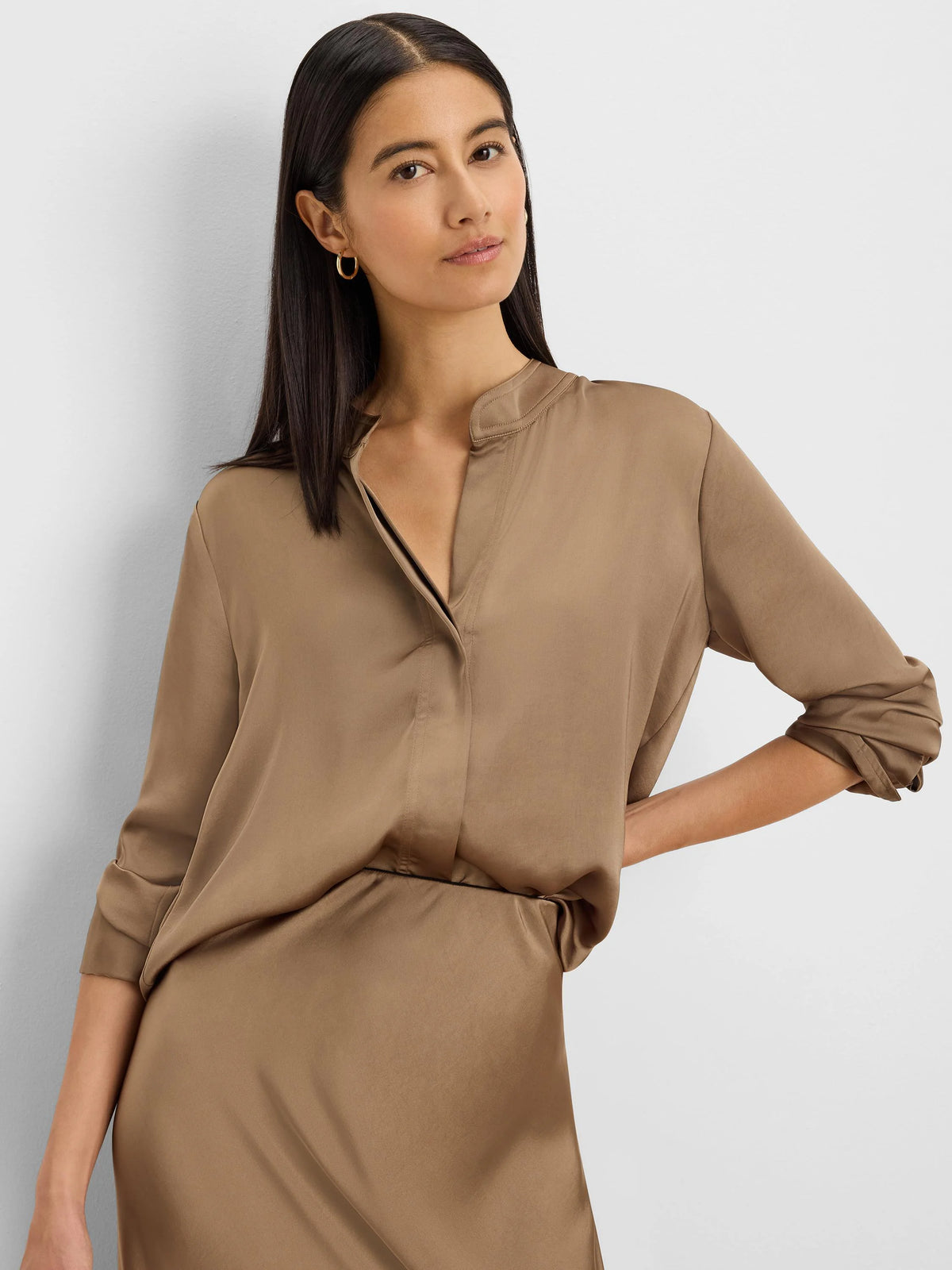 Tan glossy shirt featuring a band collar, V-neck opening, and rolled-up long sleeves. Smooth, silky fabric texture.