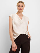 Cream, glossy tee with a draped V-neck and cap sleeves.