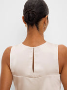 Back of a glossy, light beige woven tank top. Features a keyhole opening and button closure at the back of the neck.