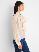 Cream crinkle-textured top with a large neck tie bow, long sleeves, and buttoned cuffs.