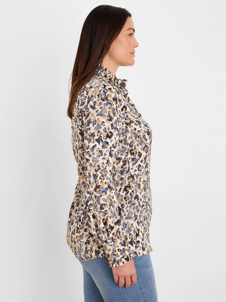 Woman wearing a cream shirt with ruffled collar and cuffs, featuring an abstract blue, gold, and dark grey 'flake' pattern.