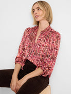 Red-orange geometric patterned shirt with smocked shoulders, mandarin collar, and vertical pleats.