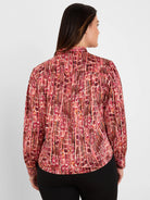 Back view: Shirt with red, orange, black abstract vertical pattern and extensive pleating. Long sleeves.