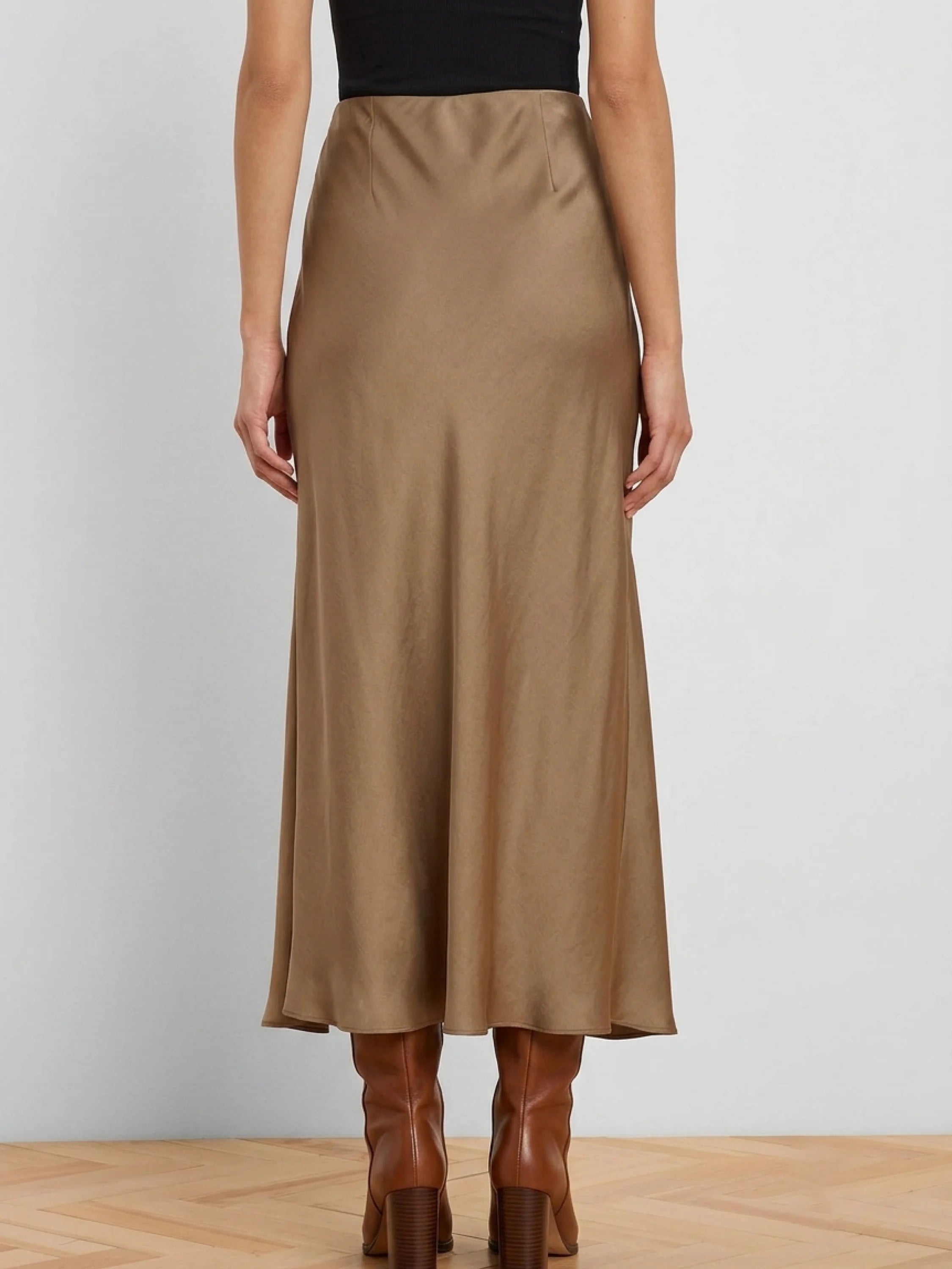 Back view of a light brown, glossy slip skirt. It's midi length with a subtle sheen, worn with a black top and brown boots.
